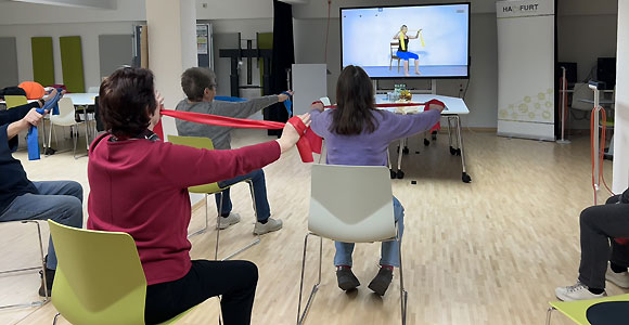 Leichte Übungen im Sitzen mit dem Theraband – angeleitet über ein Online-Video im Stadtlabor Haßfurt konnten die Teilnehmenden von „MIT & FIT – Begegnung durch Bewegung“ neue Übungen und Bewegungselemente kennenlernen. (Foto: Friederike Schulz / MGH)